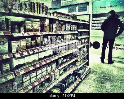 Avvia il farmacista, interno, ben rifornita ripiani con una varietà di farmaci OTC e di una persona in piedi al bancone per raccogliere una prescrizione Foto Stock