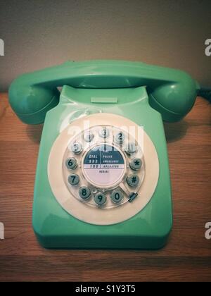 Un vecchio stile, in stile retrò telefono con ricevitore e quadrante circolare in verde e su un sfondo di legno Foto Stock