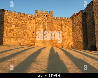 Castillo de Trujillo, la Spagna, la parete del fort antico al tramonto. Le ombre degli alberi visibile in primo piano. Foto Stock