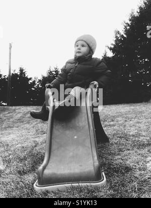 Immagine in bianco e nero di toddler ragazza seduta sulla slitta di plastica nel giardino sul retro Foto Stock