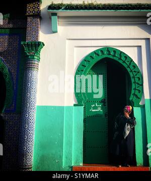 Una donna sta in piedi di fronte ad una porta verde a Tangeri, Marocco, Africa Foto Stock
