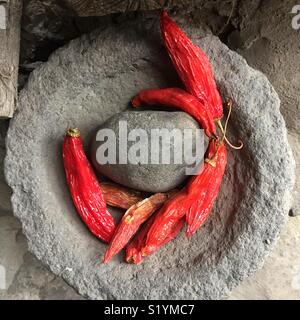 Red Hot Chili Peppers in mortaio di pietra pestello pronto per essere preparato come un ingrediente in cucina. Guardando verso il basso sul peperoncino rosso in mortaio di pietra pestello. Foto Stock