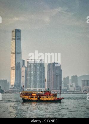 Il 'ala su Travel', un double decker giunca Cinese, portando i turisti in una crociera turistica sul Victoria Harbour al crepuscolo, di fronte alla Corte penale internazionale, Hong Kong grattacielo più alto del, nel West Kowloon Foto Stock