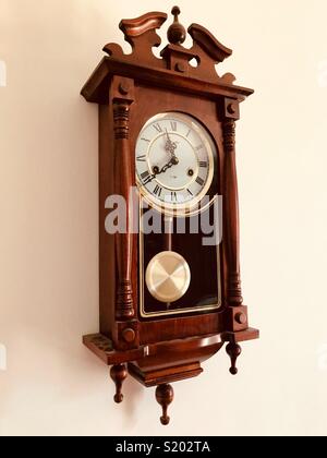 Antichi pendolo marrone orologio in legno appesi al muro bianco Foto Stock