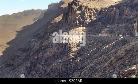 Vista su aspre rocce dei monti sull'isola delle Canarie di Gran Canaria nel sole del pomeriggio. Una strada conduce sulla ripida montagna nella valle. Foto Stock