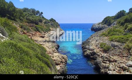 Un fiume Azzurro scorre tra le rocce e alberi verdi sulla costa di Maiorca nel Mare Mediterraneo Foto Stock