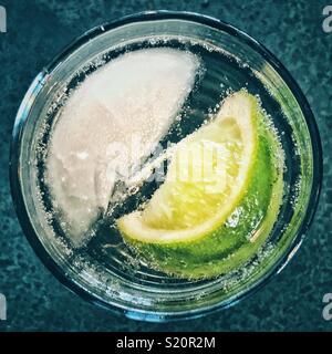 Vista dall'alto di un singolo cubo di ghiaccio e uno spicchio di lime in un bicchiere di acqua frizzante Foto Stock