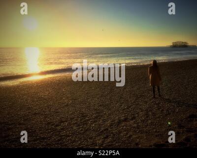 Donna in piedi sulla spiaggia al tramonto Foto Stock