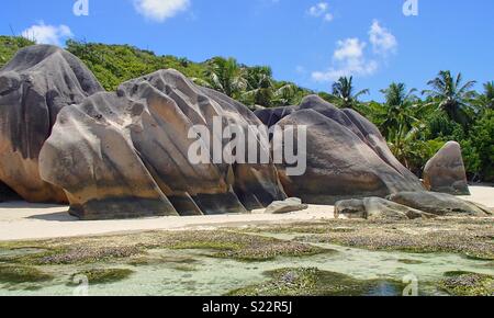 Tipica formazione rocciosa con tracce di erosione sulla spiaggia nelle Seychelles. Tre massi sulla spiaggia di sabbia bianca di fronte alla campagna verde e blu cielo Foto Stock