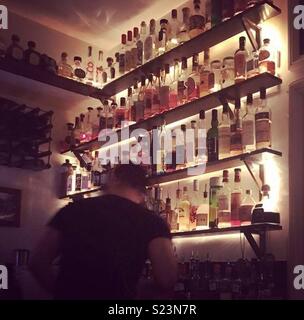 Il Barman nella parte anteriore degli scaffali di bottiglie in un piccolo bar Foto Stock