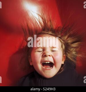 Il Toddler ragazza ridere con gioia come lei scorre una slitta rossa Foto Stock