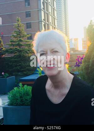 Donna matura con i capelli grigi sorridenti sulla falda di tetto a midtown Manhattan, New York, Stati Uniti d'America Foto Stock