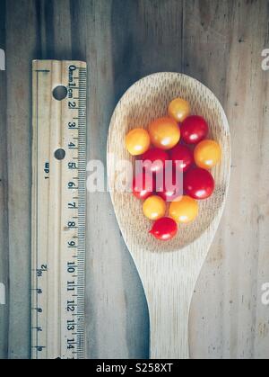 Rosso e giallo Tomberry pomodori in un cucchiaio di legno accanto a un righello per illustrare le loro piccole dimensioni Foto Stock