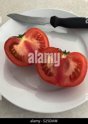 Rosso pomodoro tagliato a metà sulla piastra con il coltello Foto Stock