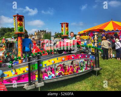 Giostre bambini su un merry-go-round e un lato gioco di stallo all'annuale Sherborne Castle Country Fair, Sherborne, Dorset, Inghilterra Foto Stock