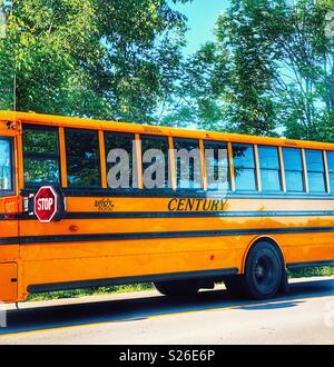 Secolo scuola bus con il segnale di arresto fuori sulla strada di campagna con l'azzurro del cielo e il verde degli alberi che riflettono in Windows Foto Stock