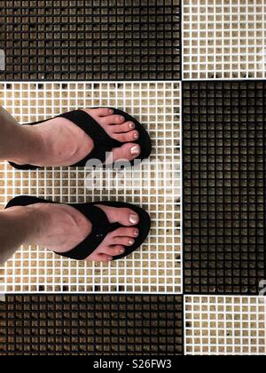 Piedi in flip-flop su un bianco e nero piano. Foto Stock