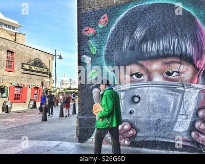 Un uomo cammina passato un murale esterno Wagamama's restaurant il Clink Street a Londra, Inghilterra.St Pauls Cathedral può essere visto nella skyline Foto Stock