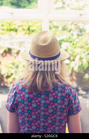 Vista posteriore di una giovane ragazza in un bel vestito floreale e cappello di paglia Foto Stock