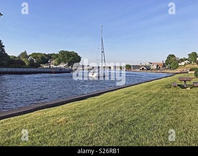 South Haven, Michigan, Stati Uniti d'America - 8 Giugno 2018: una barca a vela che viaggiano fino il fiume nero verso il porto in Sud Haven, Michigan, Stati Uniti d'America al di fuori del lago Michigan con blue sky copia spazio. Foto Stock
