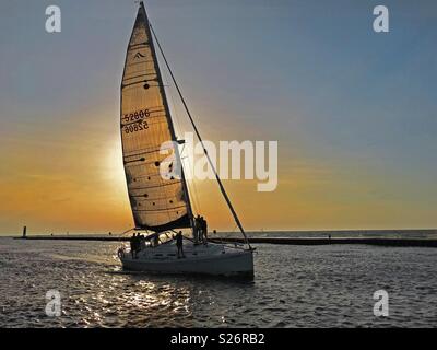 South Haven, Michigan, Stati Uniti d'America - 8 Giugno 2018: una barca a vela al tramonto che viaggiano fino il fiume nero dal Lago Michigan verso il porto in Sud Haven, Michigan, Stati Uniti d'America con blue sky copia spazio. Foto Stock
