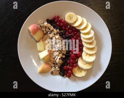 Vista in elevazione su cereali e frutta fresca per il muesli colazione sulla piastra bianca Foto Stock