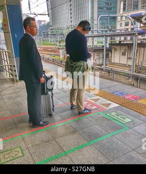 Due uomini giapponesi in attesa in linea su una piattaforma del treno a Tokyo. Foto Stock