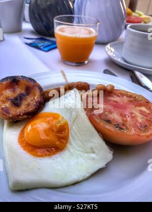 Colazione cucinata. Uovo fritto, pomodoro, salsicce, fagioli al forno, hash brown, tè, succo di arancia, Foto Stock