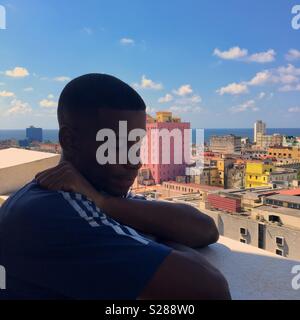 Locale uomo cubano su un balcone che guarda triste chiudendo gli occhi con l'Avana edifici e mare in background Foto Stock