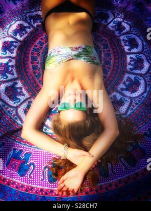 Giovane donna in bikini a prendere il sole sul vivacemente colorato asciugamano Foto Stock