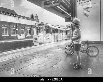 Un ragazzo con la sua moto guardando il Giubileo che si avvicina il treno di linea, Londra Foto Stock