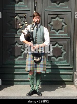 Giovane uomo giocando una zampogna e vestito con un kilt sulle strade di Edimburgo, Scozia Foto Stock