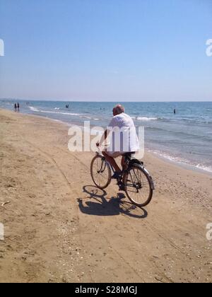 Il vecchio uomo ciclismo su Carnon beach, Mauguio, Francia Occitanie Foto Stock