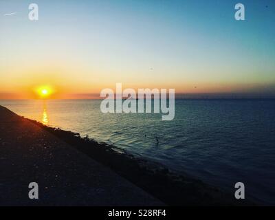 Tramonto al mare a parete, Herne Bay. Il molo vecchio a distanza Foto Stock