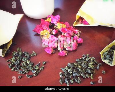 Due piastrelle di tè verde cinese e boccioli di rosa su un tavolo. Foto Stock
