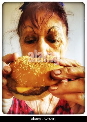 Donna anziana mangiare formaggio hamburger Foto Stock
