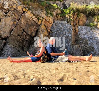 Una coppia di mezza età lettura su una spiaggia a Tenby, West Wales. Foto Stock