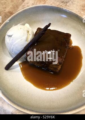 Ciotola di sticky toffee pudding con gelato alla vaniglia e salsa Foto Stock