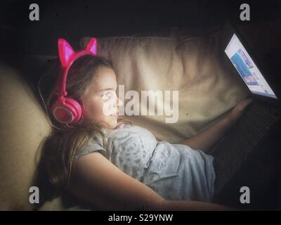 11 anno vecchia ragazza indossando illumina neon pink cuffie guardare i video su un computer portatile Foto Stock