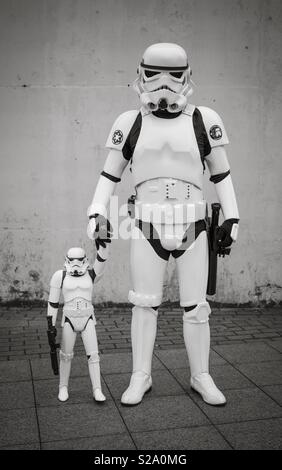 Un maschio cosplayer vestito come un Stormtrooper dei film di Star Wars tiene per mano un bambino piccolo anche in un costume Foto Stock