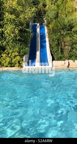 Doppio scivolo d'acqua in crystal clear piscina circondata da alberi. Foto Stock