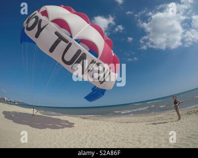 Un parapendio cartoleria su una spiaggia con una signora in attesa di portarlo sulla spiaggia per un fly ride Foto Stock