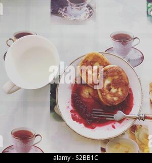 Frittelle di formaggio sulla piastra con una confettura di lamponi e una tazza di latte sul tavolo Foto Stock