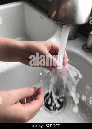 Spruzzi di acqua come un ragazzino è un lavaggio del quarzo cristalli nel lavello da cucina Foto Stock