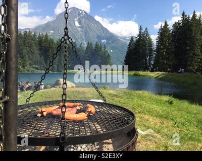 Tipicamente Svizzera Cervelat salsicce su una griglia a carbone nelle Alpi Svizzere. Arnisee, Uri, Svizzera. Foto Stock