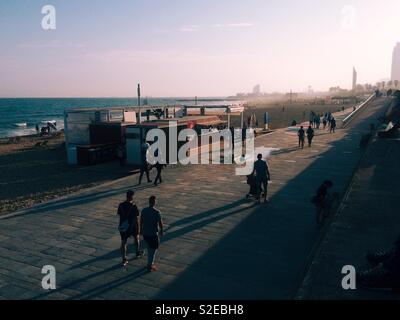 Sagome di persone che passeggiano lungo il lungomare della spiaggia di El Poblenou a Barcellona, Spagna, ammirando il tramonto in autunno Foto Stock