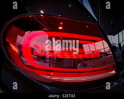 L'elegante fanalino di coda di un'automobile in mostra riflette il nuovo showroom di auto nelle scintillanti sfumature di rosso. Concetti: Interni, eleganza, riflessione, modernismo. Design elegante. Settore automobilistico. Foto Stock