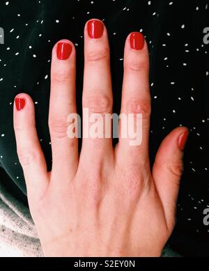 Mano femminile con il classico rosso lucido per unghie manicure test sul bianco e nero polka dot shirt Foto Stock