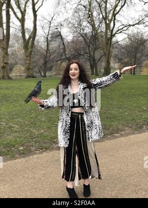 Una signora in una pelliccia trionfalmente detiene un piccione in un parco Foto Stock