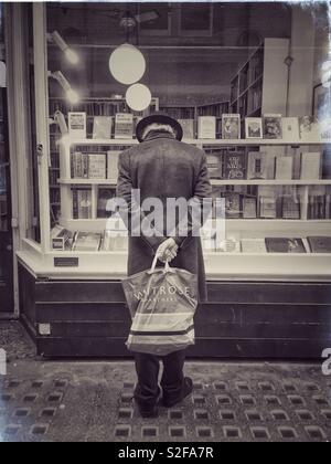 Il vecchio uomo di window shopping al di fuori di una frantumazione bookshop in Cecil Court, Londra. Foto Stock